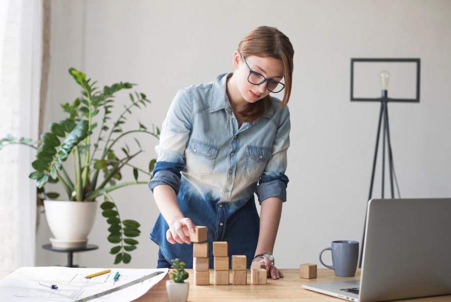 A woman building a tower of wooden blocks at her desk, representing building something from the ground up